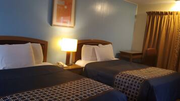 Habitación de hotel con dos camas, una mesita de noche con lámpara, una silla y un ventanal con cortinas.