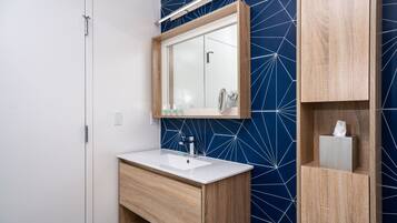 A modern bathroom with a white sink, wooden vanity, and a mirror above it.