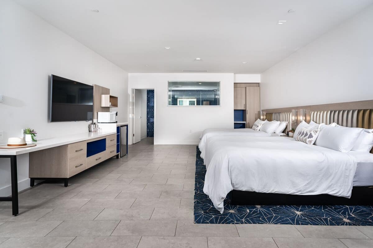 A modern hotel room with a large bed, a desk with a flat-screen TV, and a separate bathroom area.