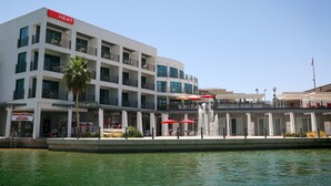 Ein mehrstöckiges Hotel mit einem 'HEAT'-Schild, Außenbestuhlung mit Sonnenschirmen und einem Wasserspiel im Vordergrund.