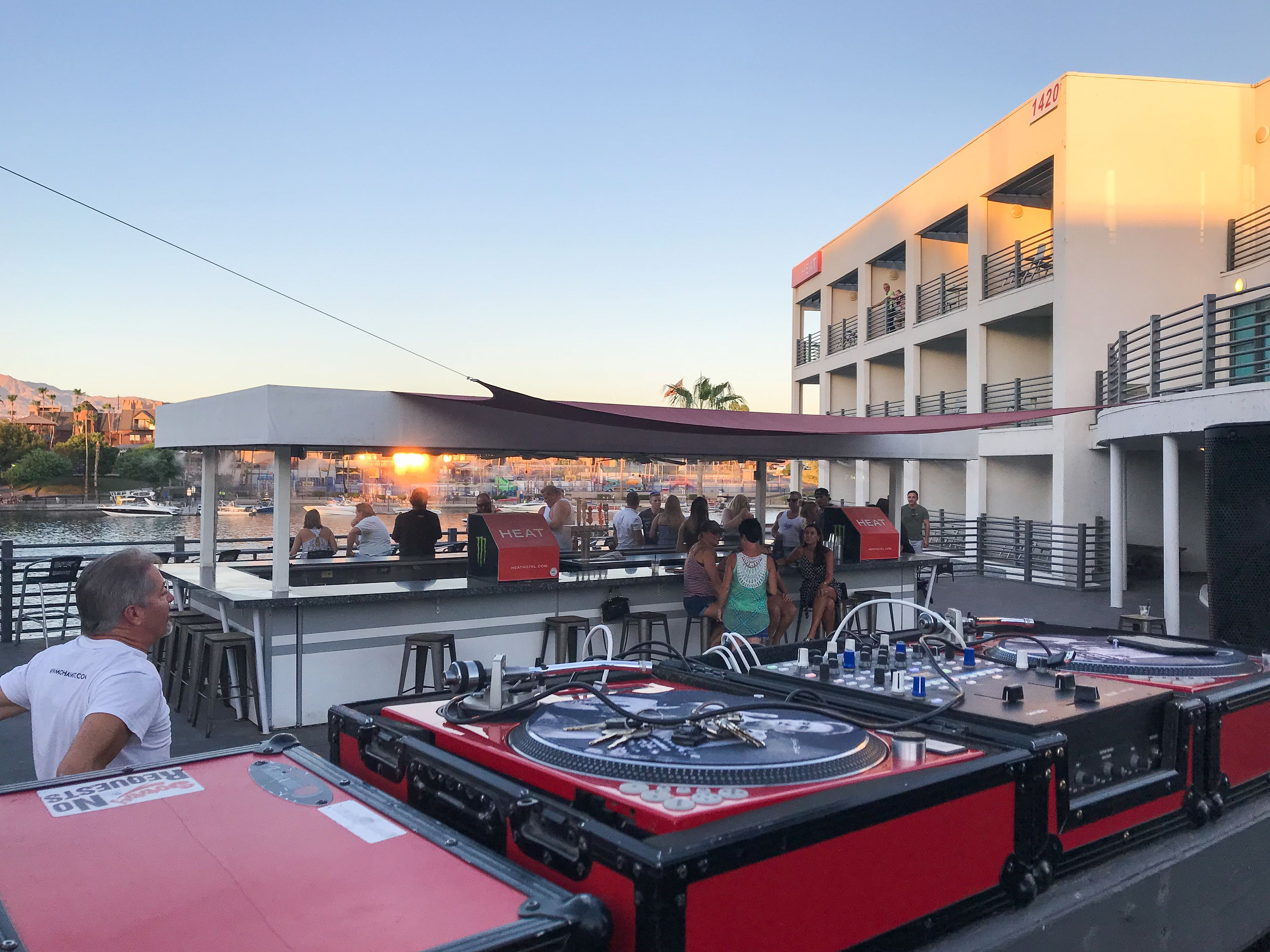 A rooftop bar with outdoor seating, a DJ setup, and a view of the cityscape.
