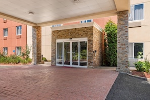 A building entrance with a brick facade, glass doors, and a paved walkway.