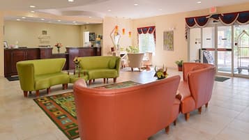 Un vestíbulo de hotel con sofás verde y naranja, un mostrador de recepción y una pared decorativa.