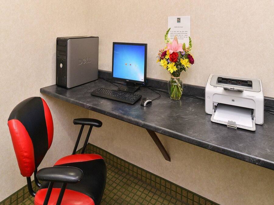 A reception desk with a desktop computer, a monitor, a keyboard, a mouse, a printer, a vase with flowers, and a red and black chair.