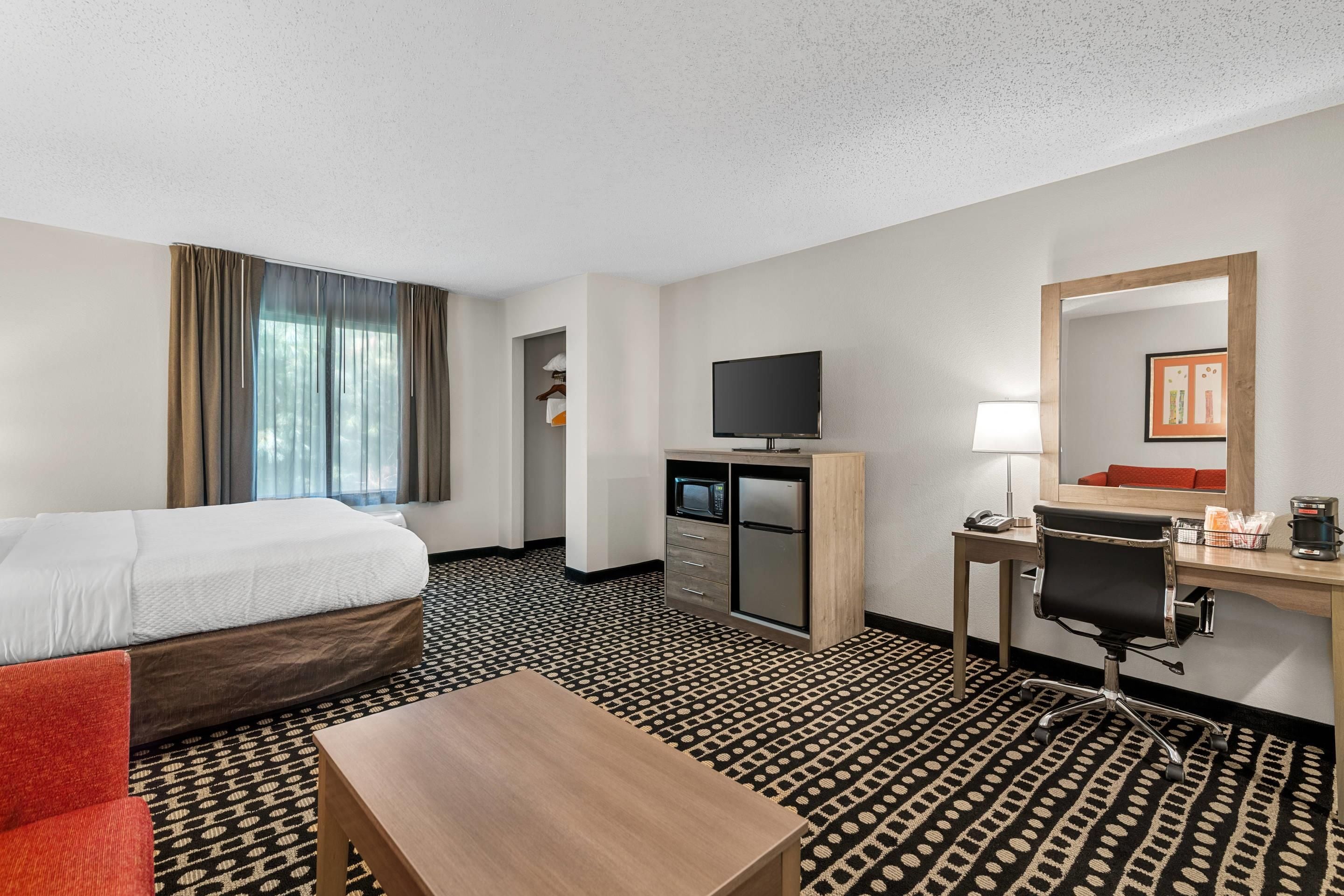 A hotel room with a bed, a desk with a computer, a television, a coffee maker, and a chair.