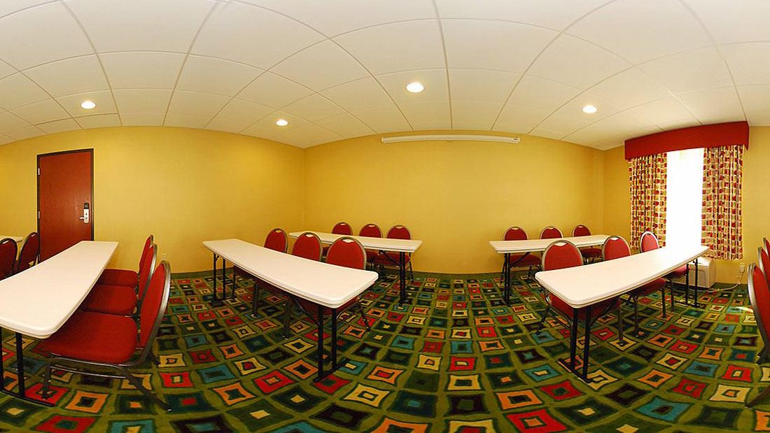 A conference room with tables and chairs, a patterned carpet, and a door.