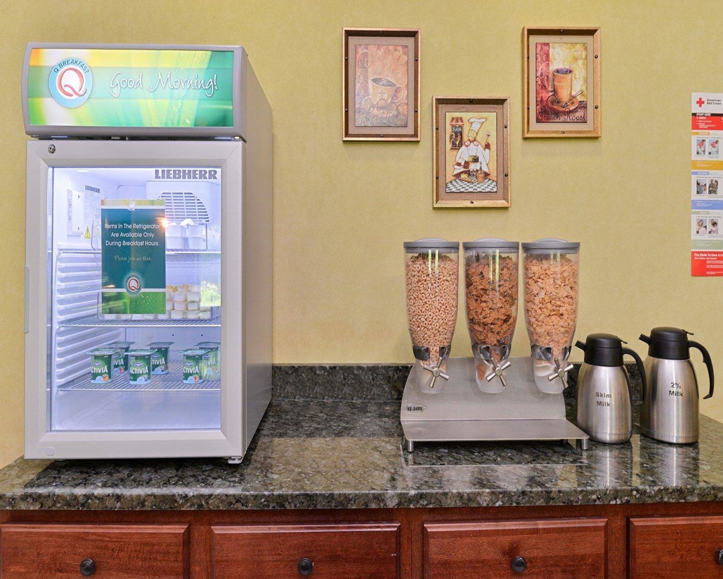 Estação de café da manhã com máquina de refrigerantes, três dosadores de leite e uma cafeteira em bancada de granito.
