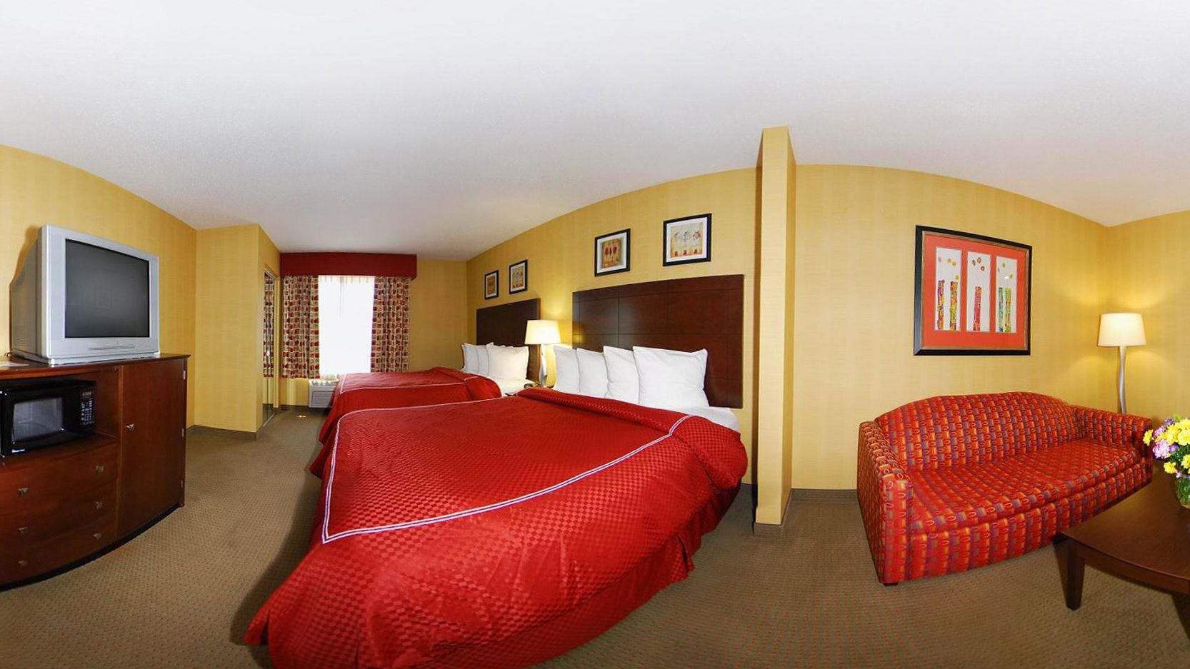 Habitación de hotel con dos camas, un televisor, un microondas, un sofá rojo y una lámpara.