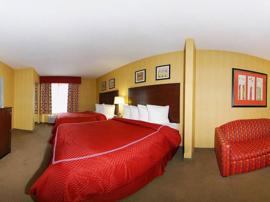 Habitación de hotel con dos camas, un televisor, un microondas, un sofá rojo y una lámpara.