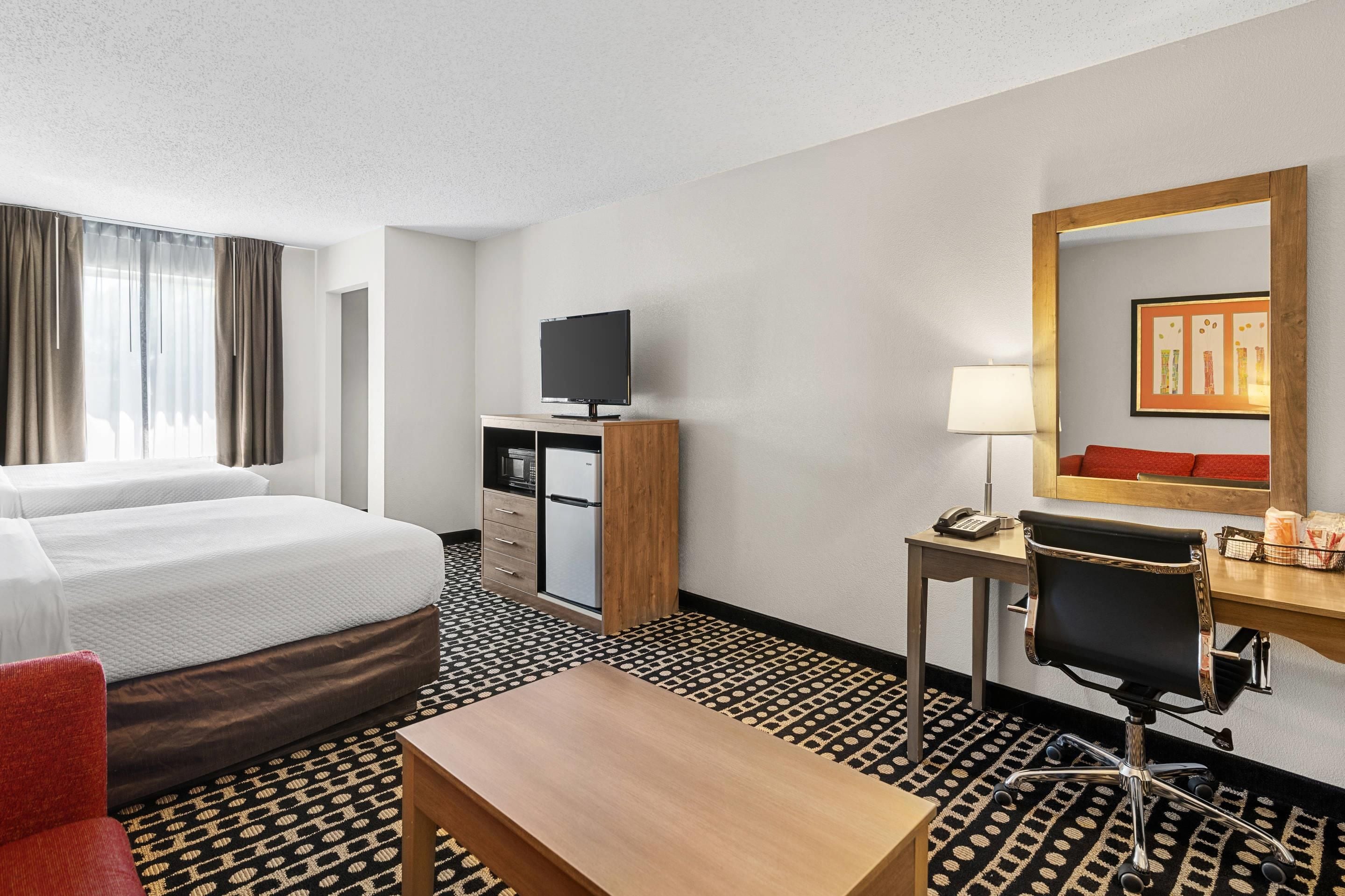 A hotel room with a bed, a desk, a chair, a television, and a mirror.