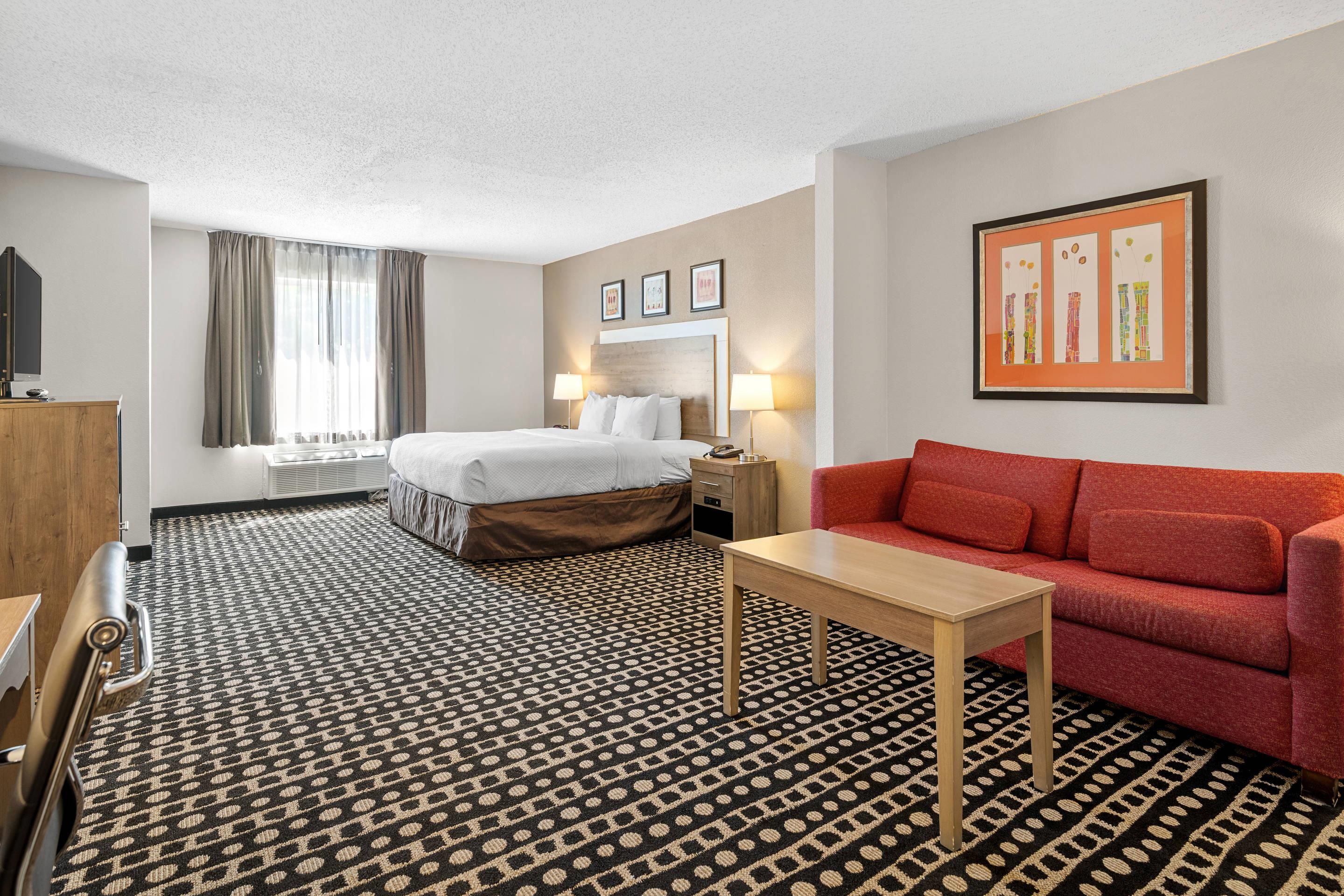 A hotel room with a bed, a red sofa, a small table, a TV, and a window with curtains.