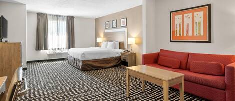 A hotel room with a bed, a red sofa, a small table, a TV, and a window with curtains.