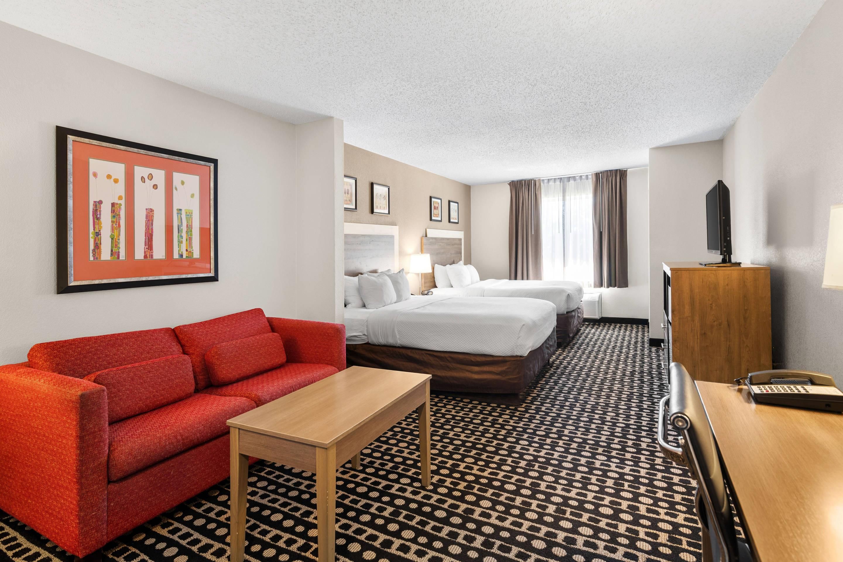 A hotel room with a red sofa, a wooden table, a bed with white bedding, a TV, and a patterned carpet.