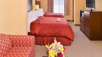 A hotel room with two beds, a TV, a desk, and a vase of flowers.