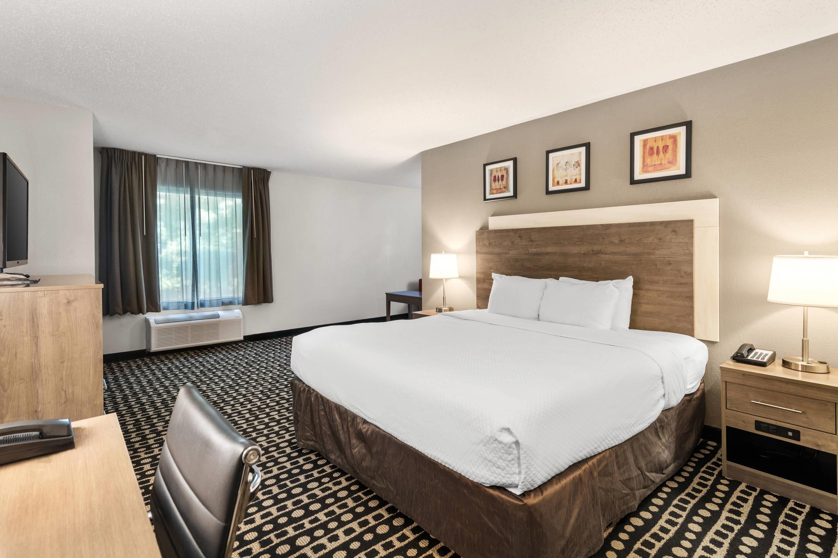 Une chambre d’hôtel avec un grand lit, un bureau avec une chaise, une télévision et une fenêtre avec des rideaux.