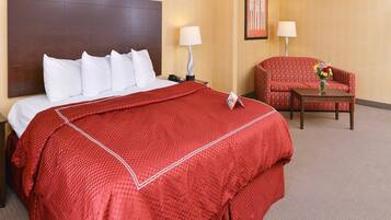 A hotel room with a large bed, a red blanket, a chair, a table, and a lamp.