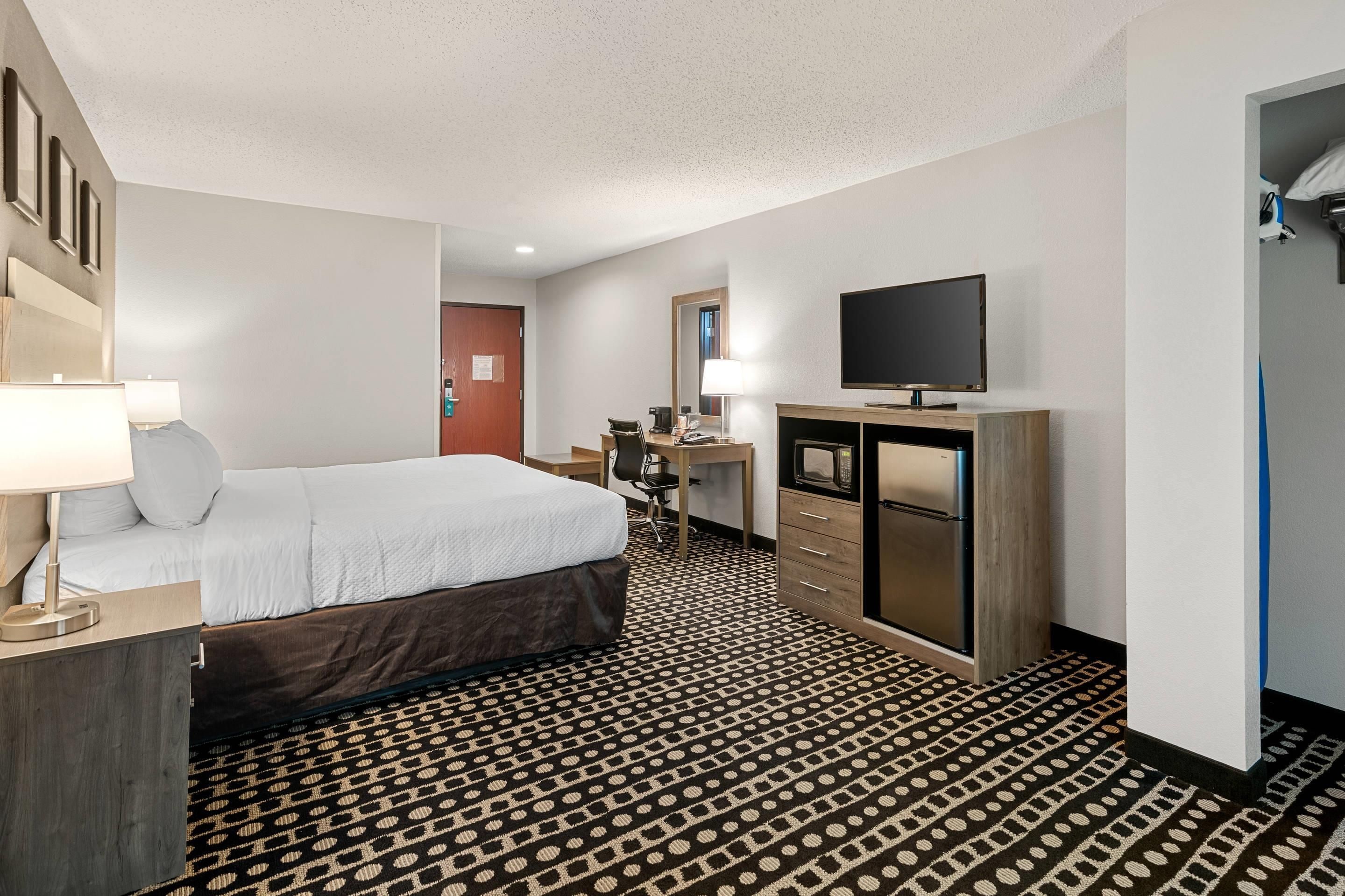 Ein Hotelzimmer mit Bett, Schreibtisch, Fernseher und einem gemusterten Teppich.