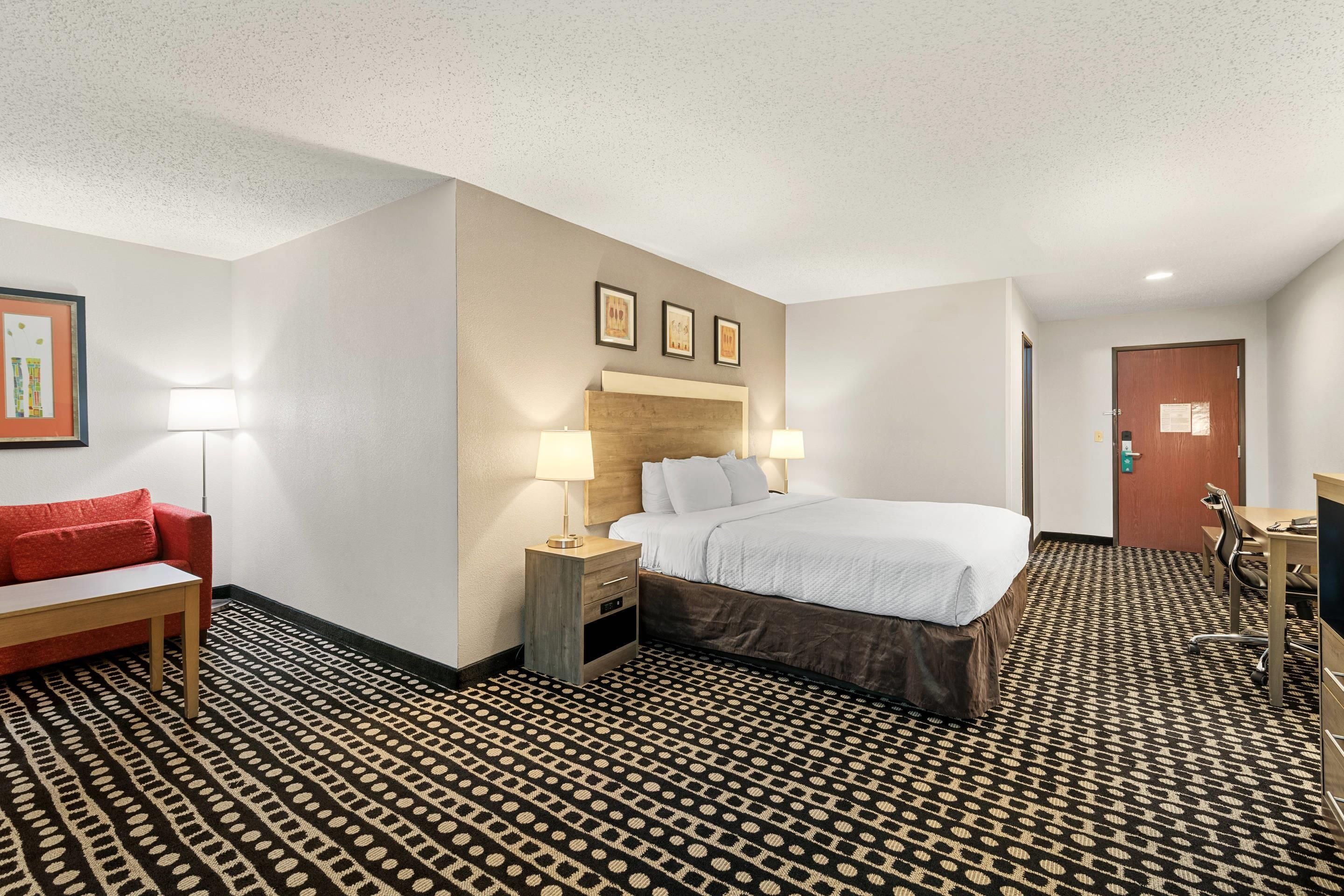 A hotel room with a bed, bedside tables, a desk, a chair, a red sofa, and patterned carpet.
