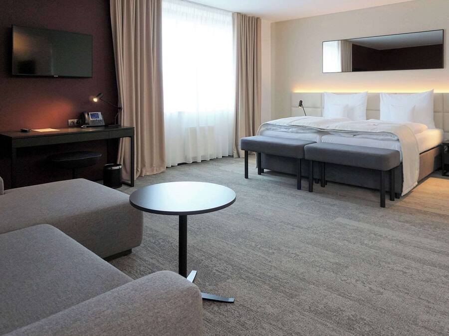 Habitación de hotel con cama, escritorio, televisor, una mesita redonda y un sofá.