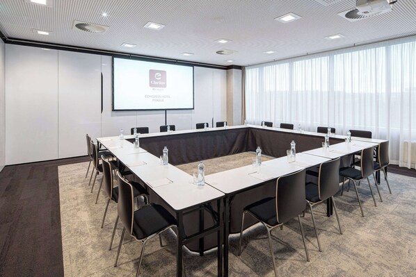 A conference room with a long table, chairs, a projector screen, and a large window with curtains.
