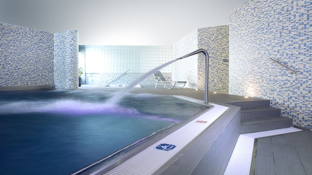 Un jacuzzi con chorro de agua, paredes de azulejos y una escalera que lleva a un nivel superior.