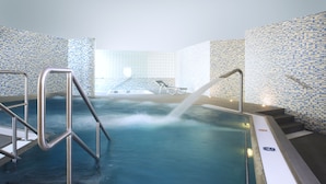Un jacuzzi con barandillas metálicas, una silla de descanso y una pared con azulejos.