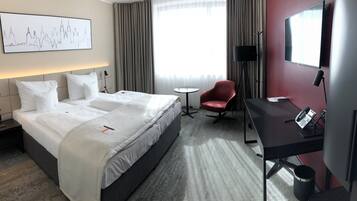 Habitación de hotel con una cama grande, un escritorio, una silla, una lámpara de escritorio, un teléfono y una ventana con cortinas.