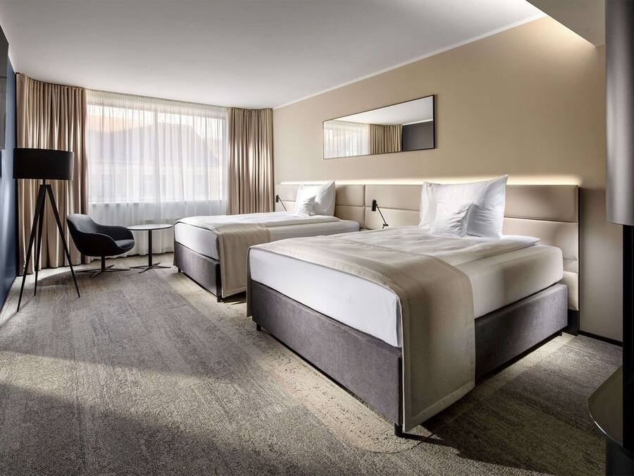 Habitación de hotel con dos camas, un escritorio, una silla, un espejo grande y una lámpara.