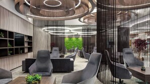 Un área de estar moderna con sillones tapizados en gris, una mesa de centro de madera con una planta y una pared verde al fondo.
