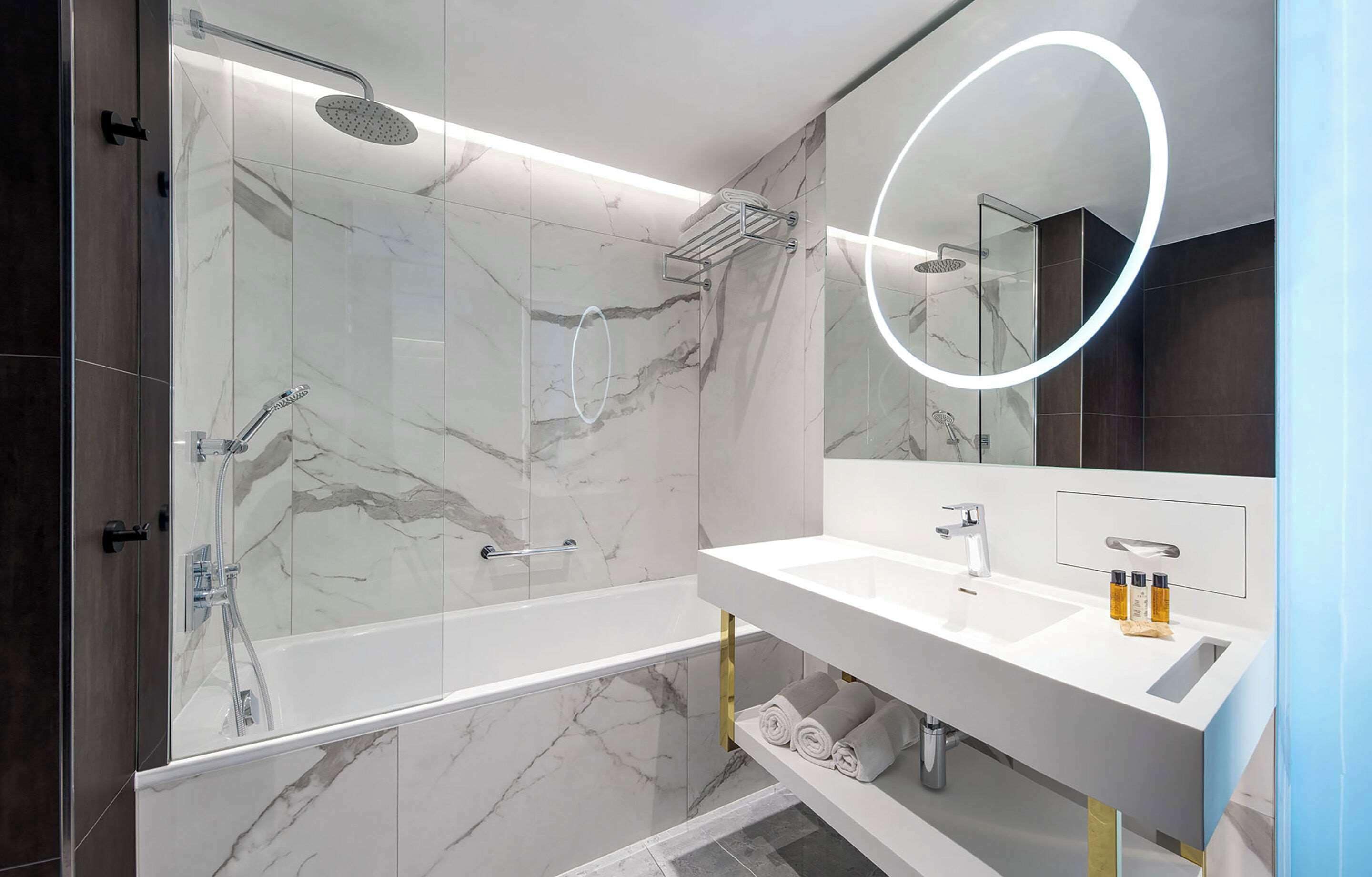 A modern bathroom with a glass-enclosed shower, a white vanity with a mirror, and marble tiles.