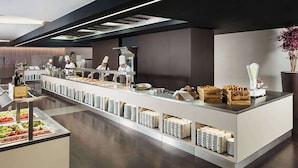 Una moderna disposición de bufé con cocineros preparando alimentos, estaciones de comida ordenadas y una variedad de platos exhibidos.