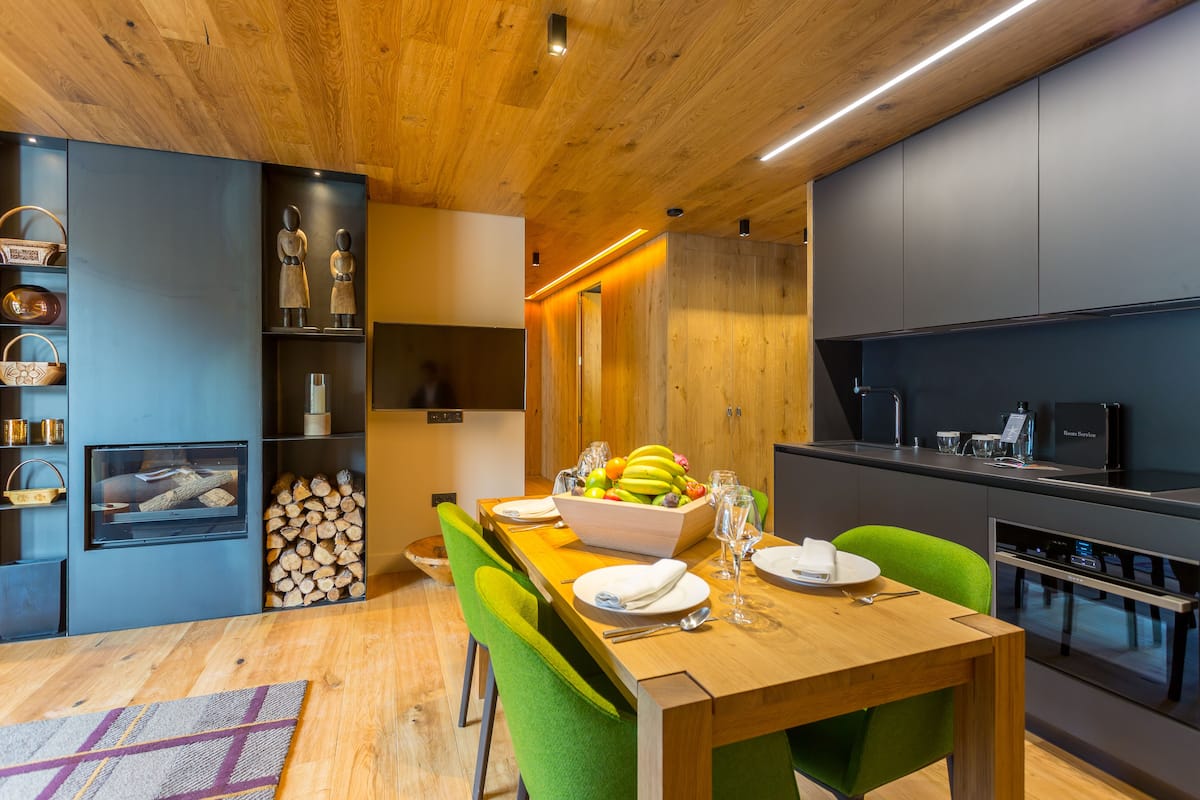 A modern kitchen with a wooden ceiling, grey cabinets, and a dining area with a wooden table and green chairs.