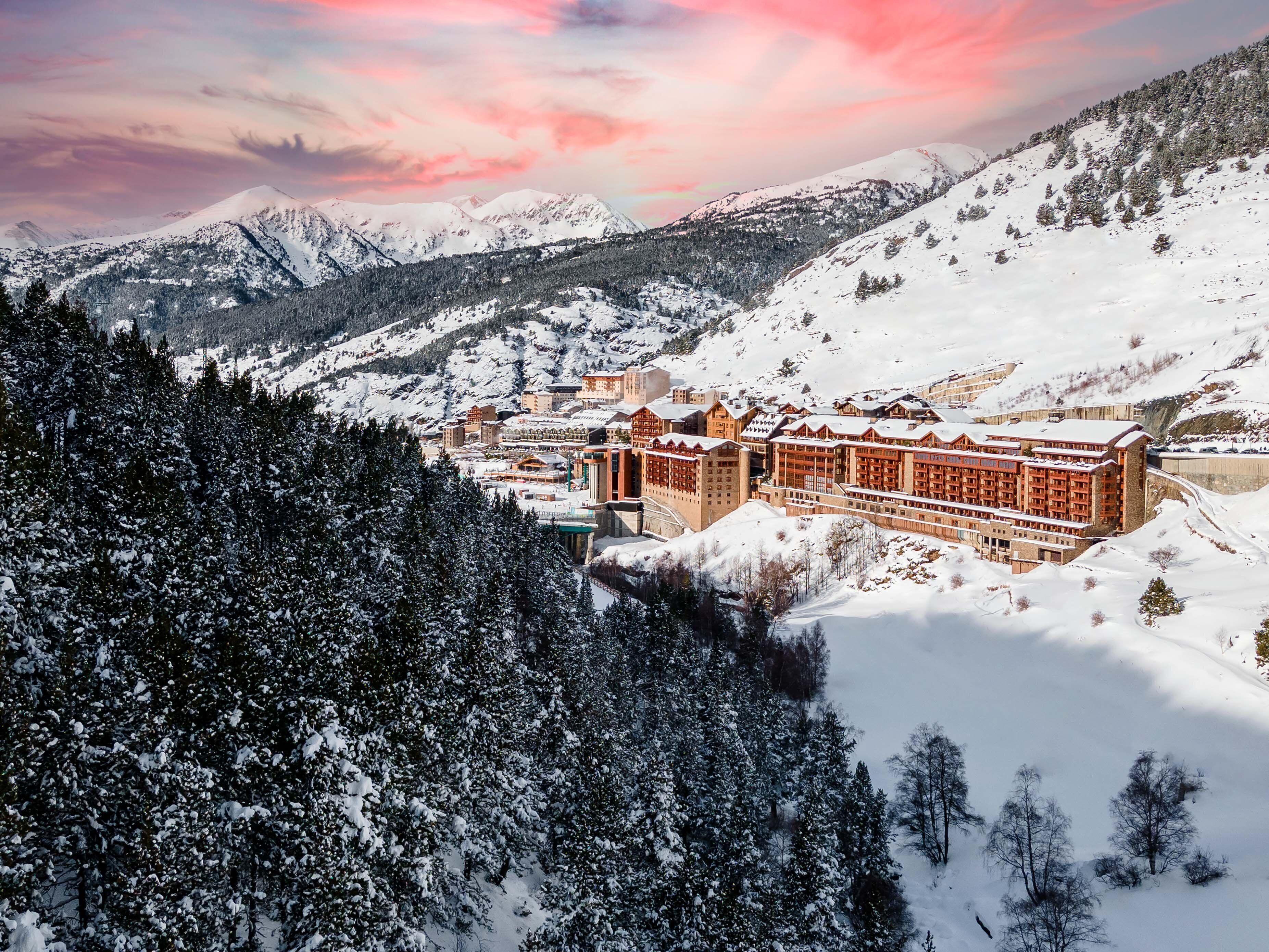 Un complejo turístico en la montaña cubierto de nieve, con un gran hotel de varios pisos y un patio central.