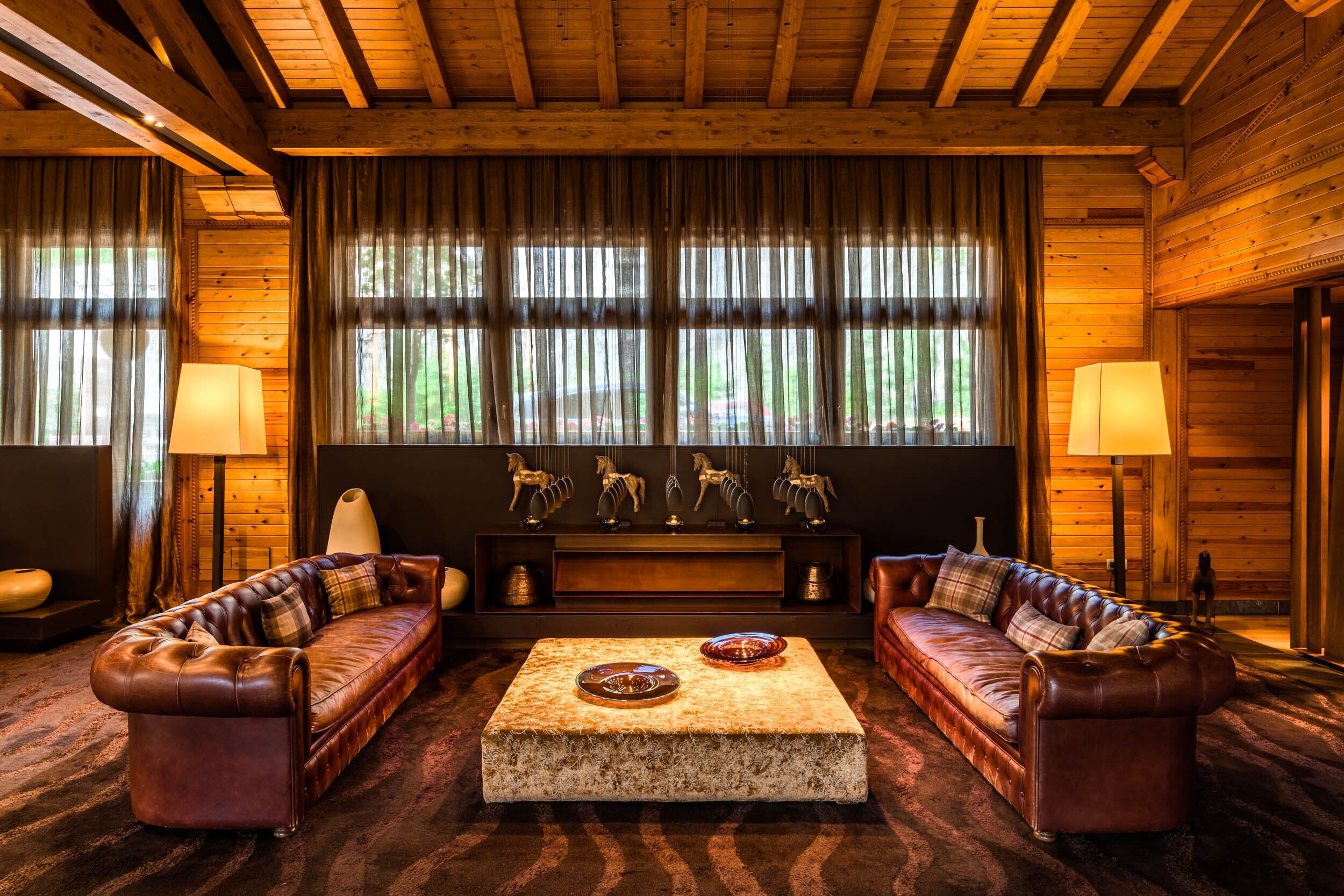 Interior acogedor de una cabaña de madera con un sofá de cuero, una mesa de centro de mármol y un banco de madera con esculturas decorativas de caballos.