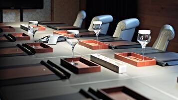 Uma mesa de conferência com vários copos de vinho e caixas retangulares, provavelmente para uma reunião ou evento.