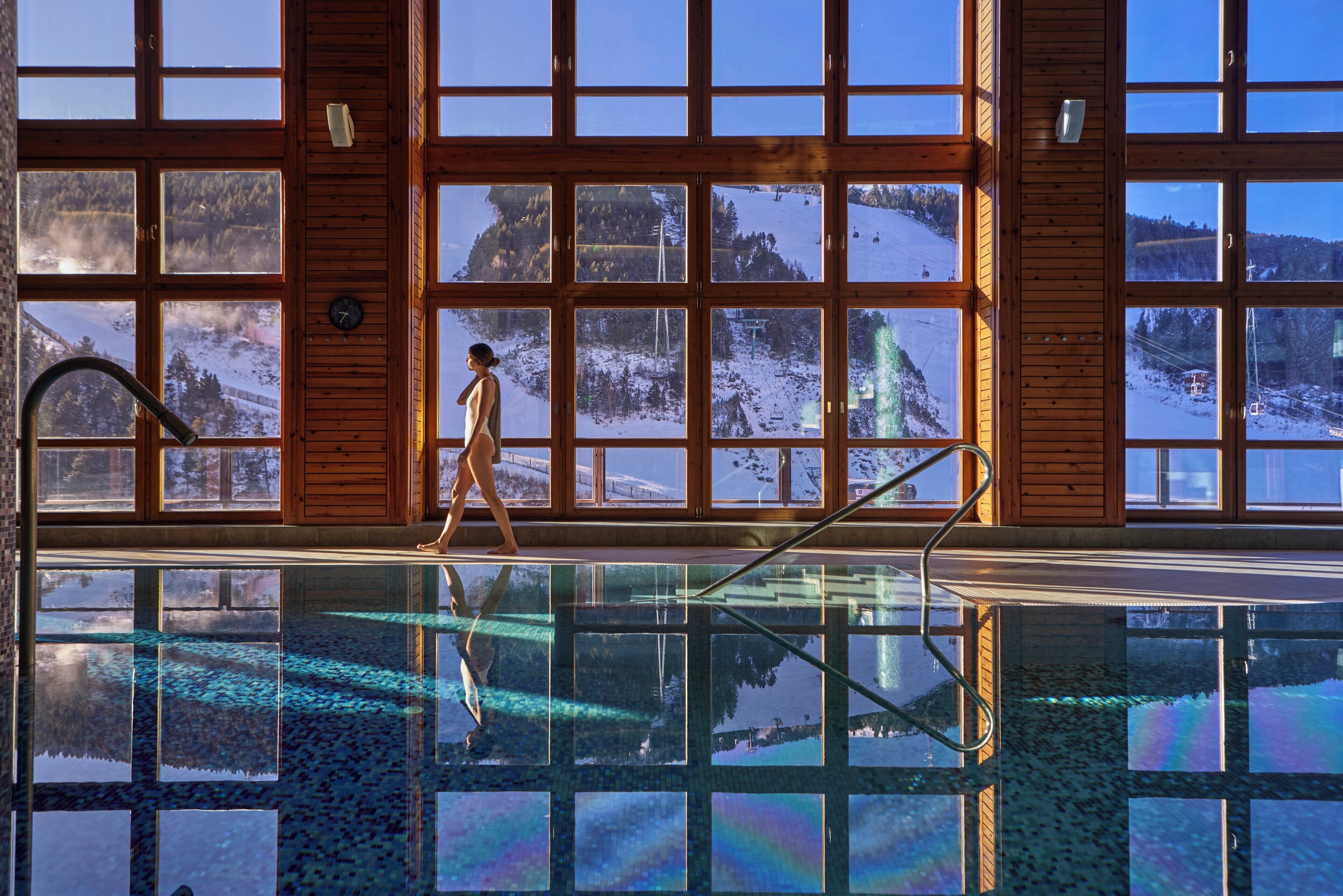 A large indoor swimming pool with clear windows offering views of a snowy mountain landscape.