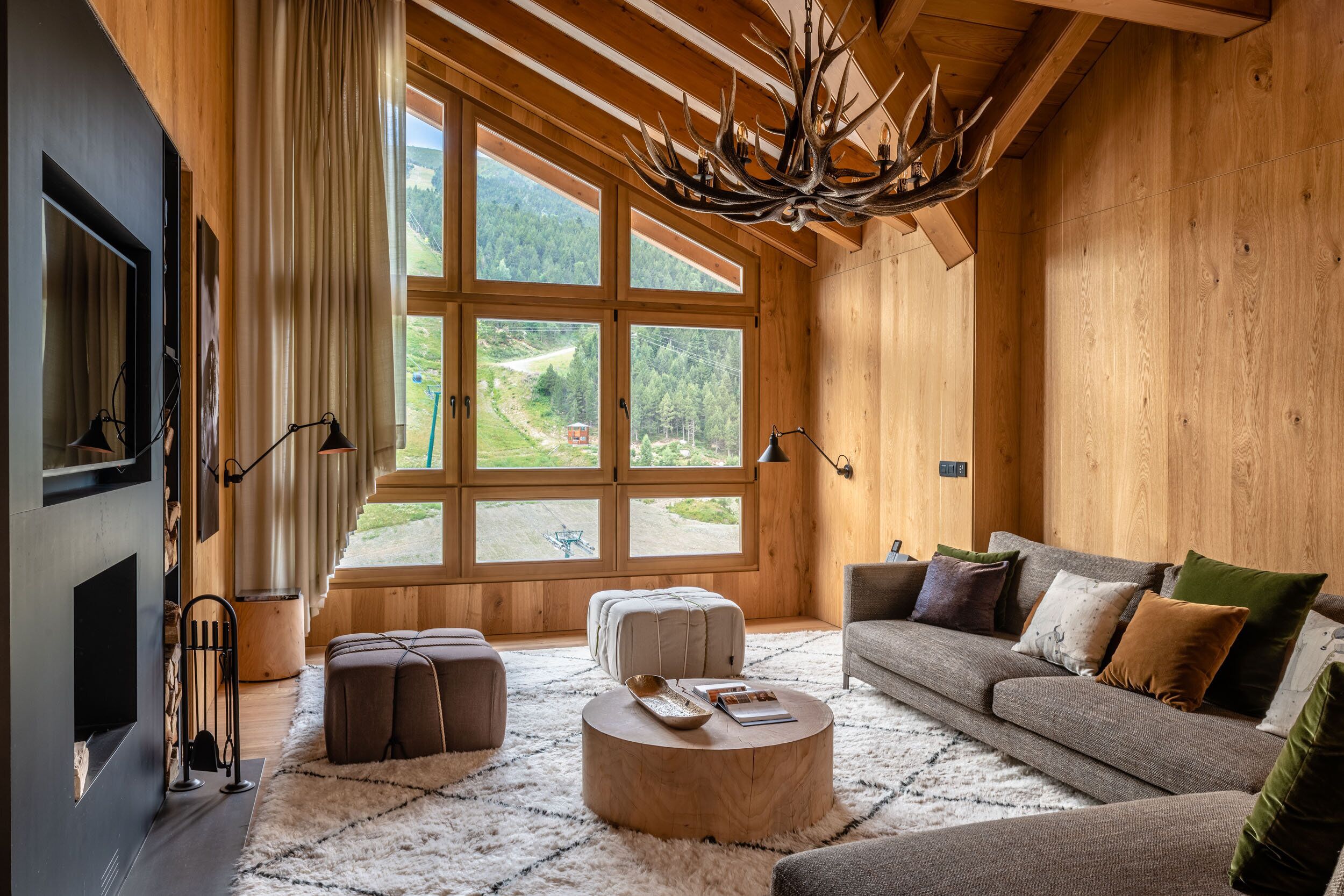 Ein gemütliches Wohnzimmer mit großem Fenster, Holzwänden, Kamin und einem einzigartigen Chandelier aus Geweihen.