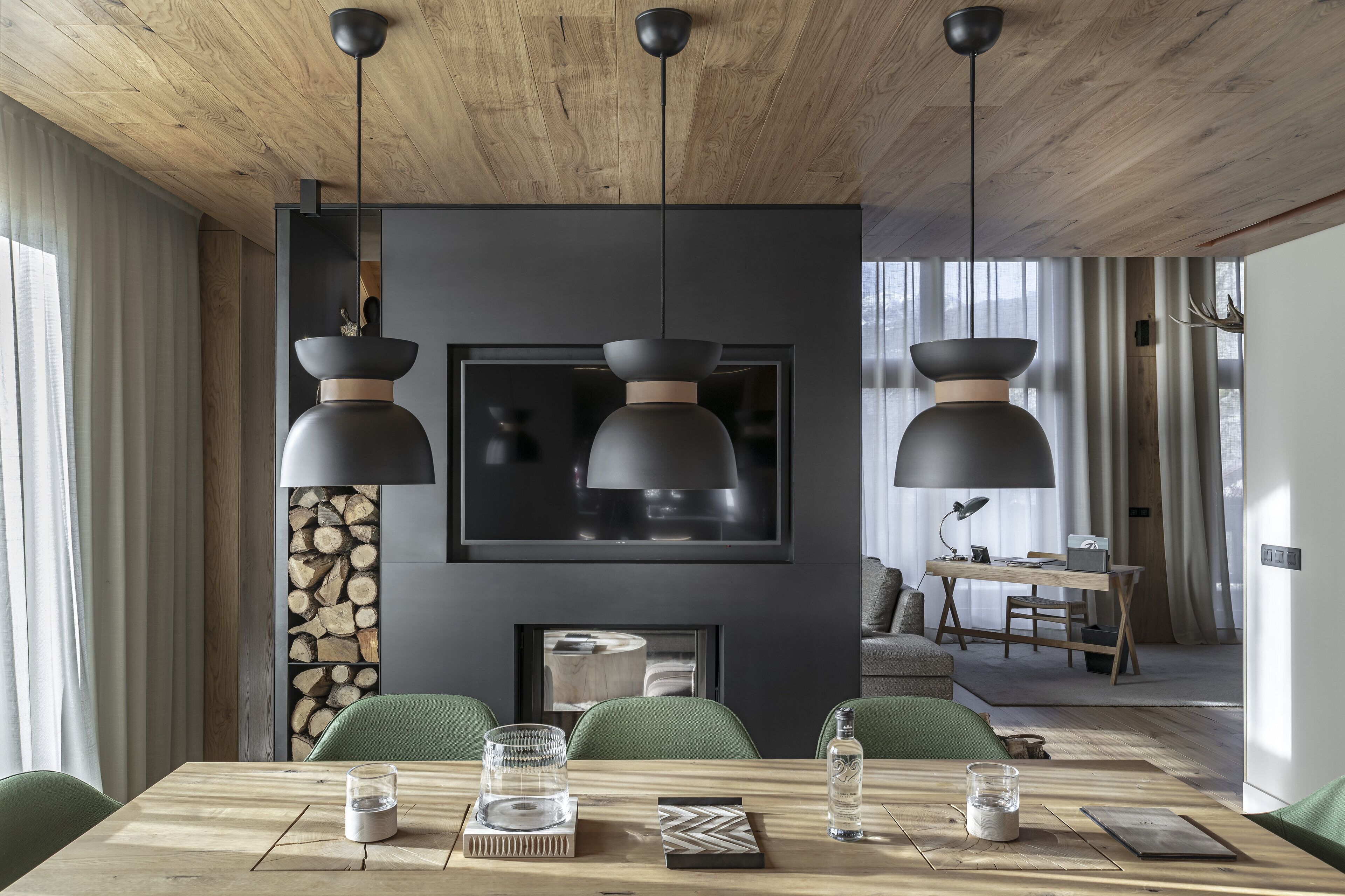 A modern dining area with a wooden table, green chairs, and pendant lights. A fireplace is visible in the background.