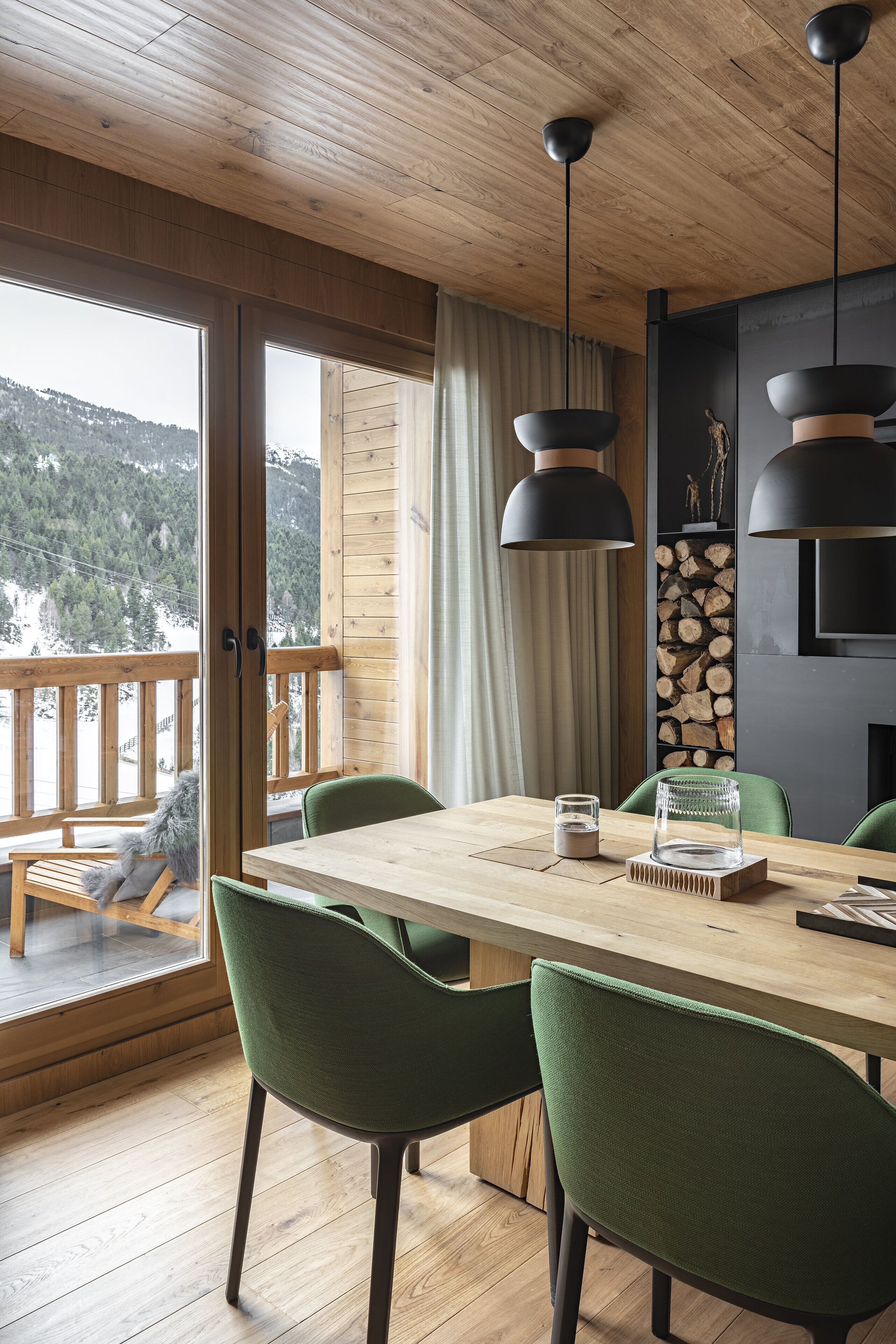 Una mesa de comedor de madera con sillas, techo de madera y vistas a un paisaje nevado a través de un ventanal.