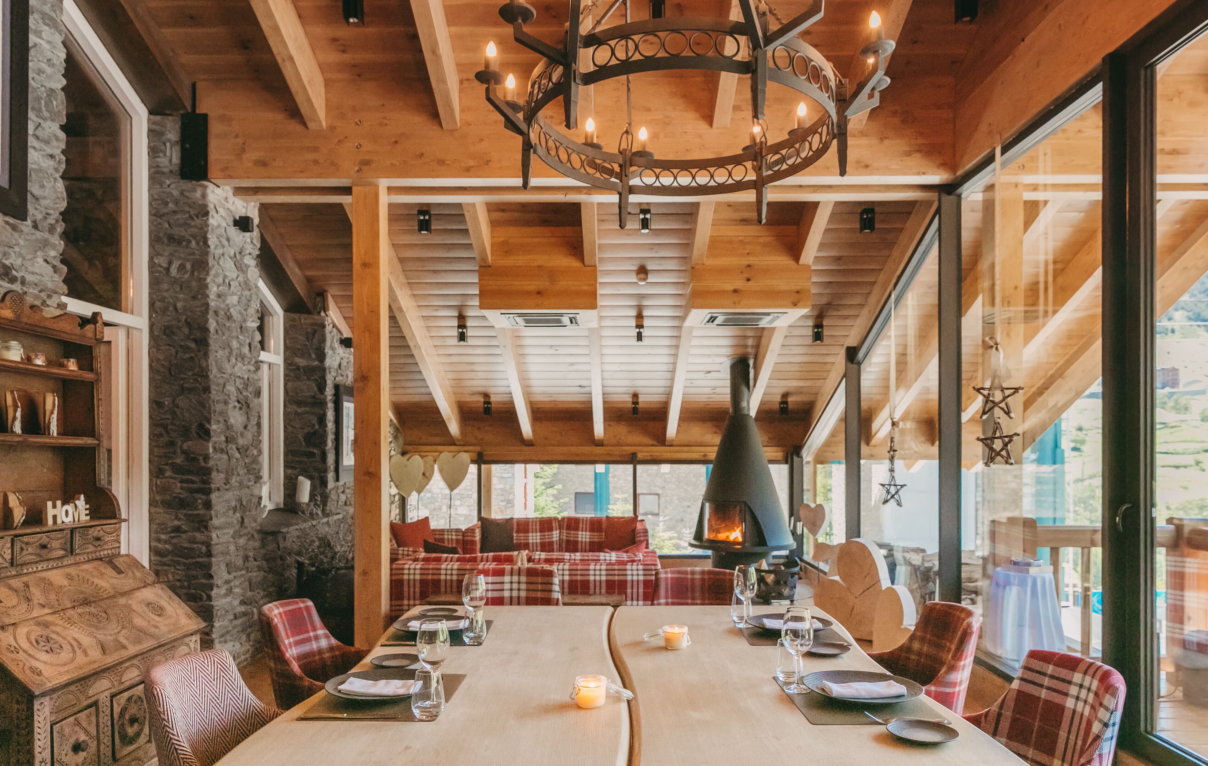 A cozy dining area with a long table set for four, a fireplace, and a stone wall on one side.