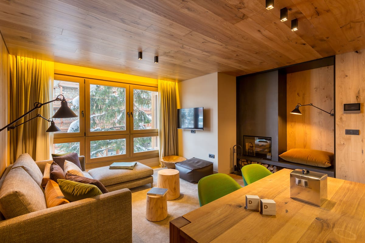 A cozy living room with a wooden ceiling, a sofa, a dining table, and a television mounted on the wall.