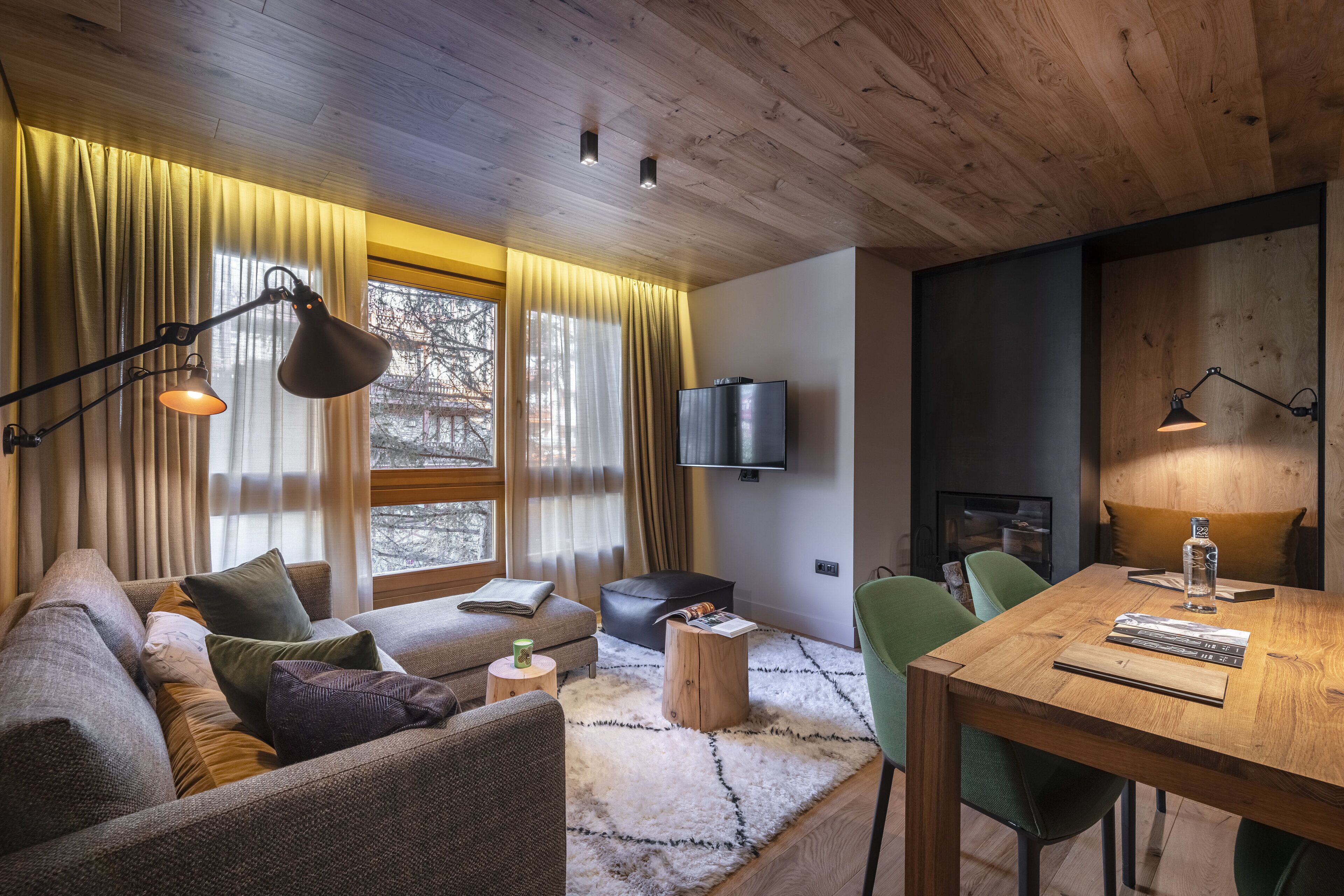 Una sala de estar acogedora con un sofá, una mesa de centro de madera, una mesa de comedor con sillas, un televisor de pantalla plana montado en la pared y una chimenea.