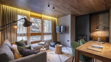 Una sala de estar acogedora con un sofá, una mesa de centro de madera, una mesa de comedor con sillas, un televisor de pantalla plana montado en la pared y una chimenea.