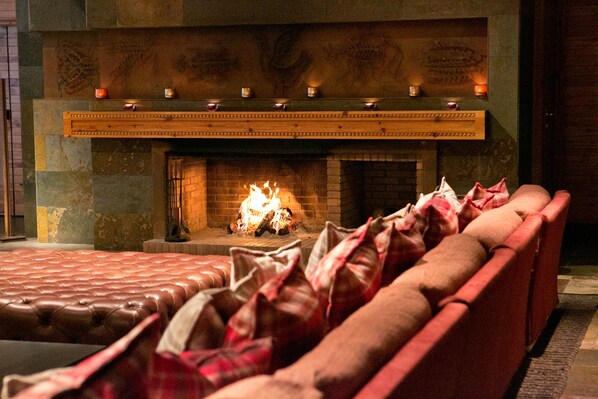 A cozy room with a brick fireplace, a leather sofa, and a row of candles. - Sport Hotel Hermitage & Spa (Soldeu)