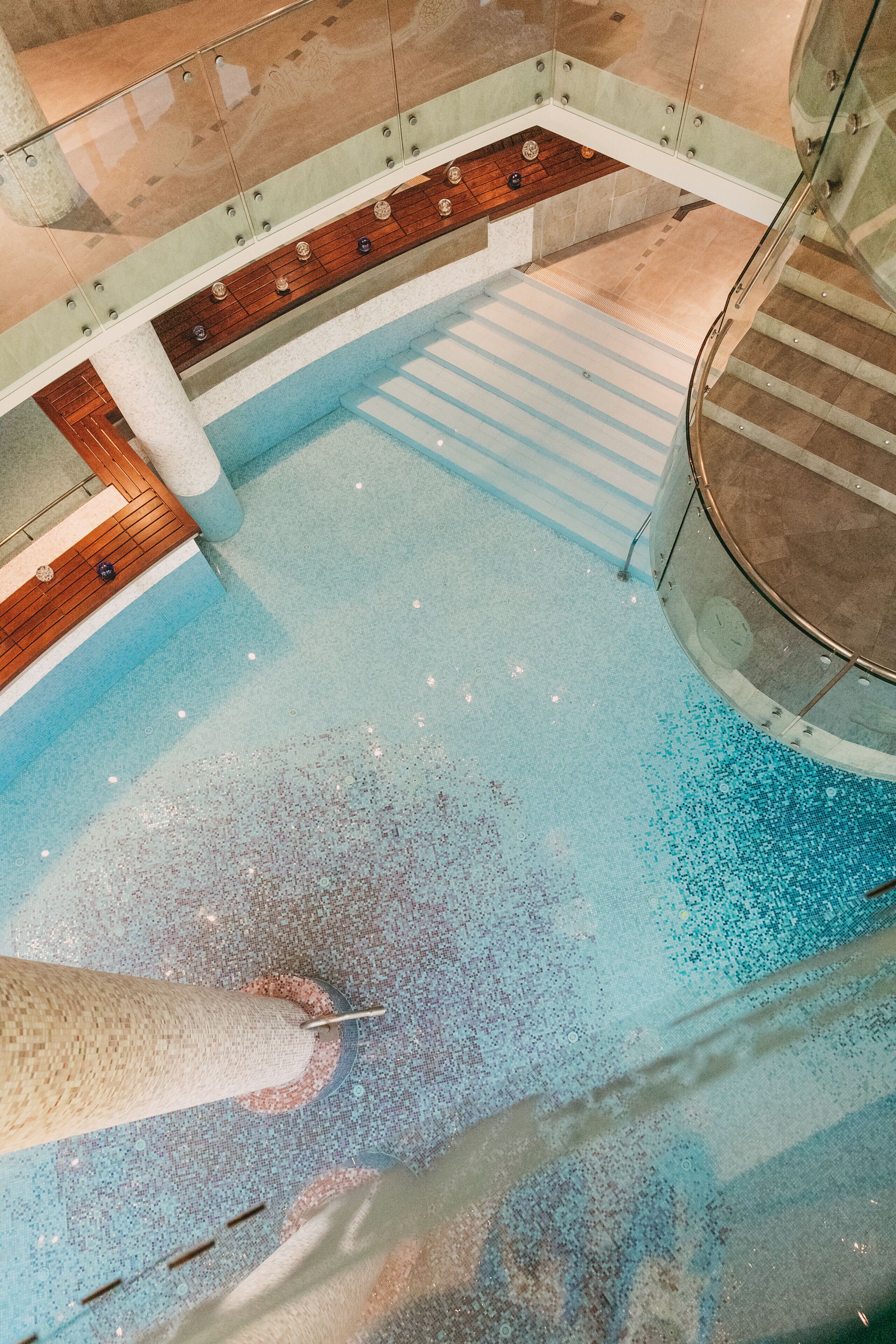 A large indoor swimming pool with a wooden deck and a glass balustrade.