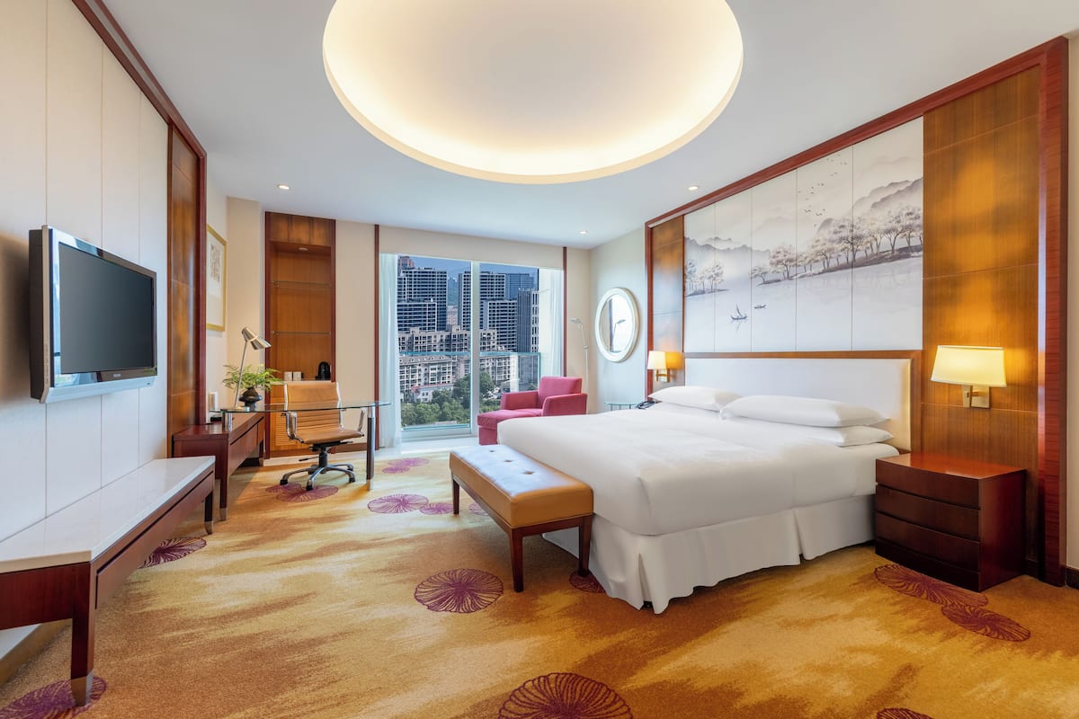 Habitación de hotel con una cama grande, un escritorio, una silla, un televisor y vistas a la ciudad.
