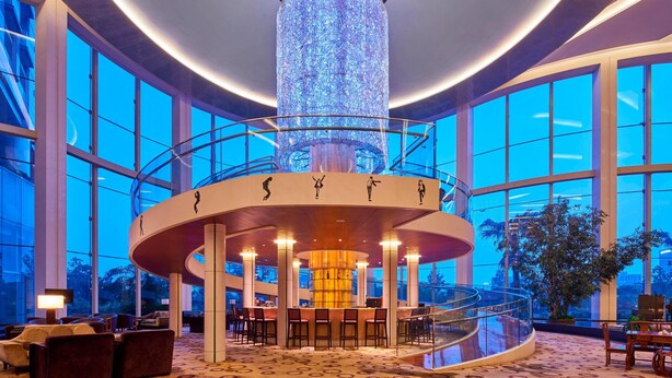 Eine großzügige Lobby mit einer zentralen zylindrischen Säule, großen Fenstern und einer Sitzgruppe in Kreisform.