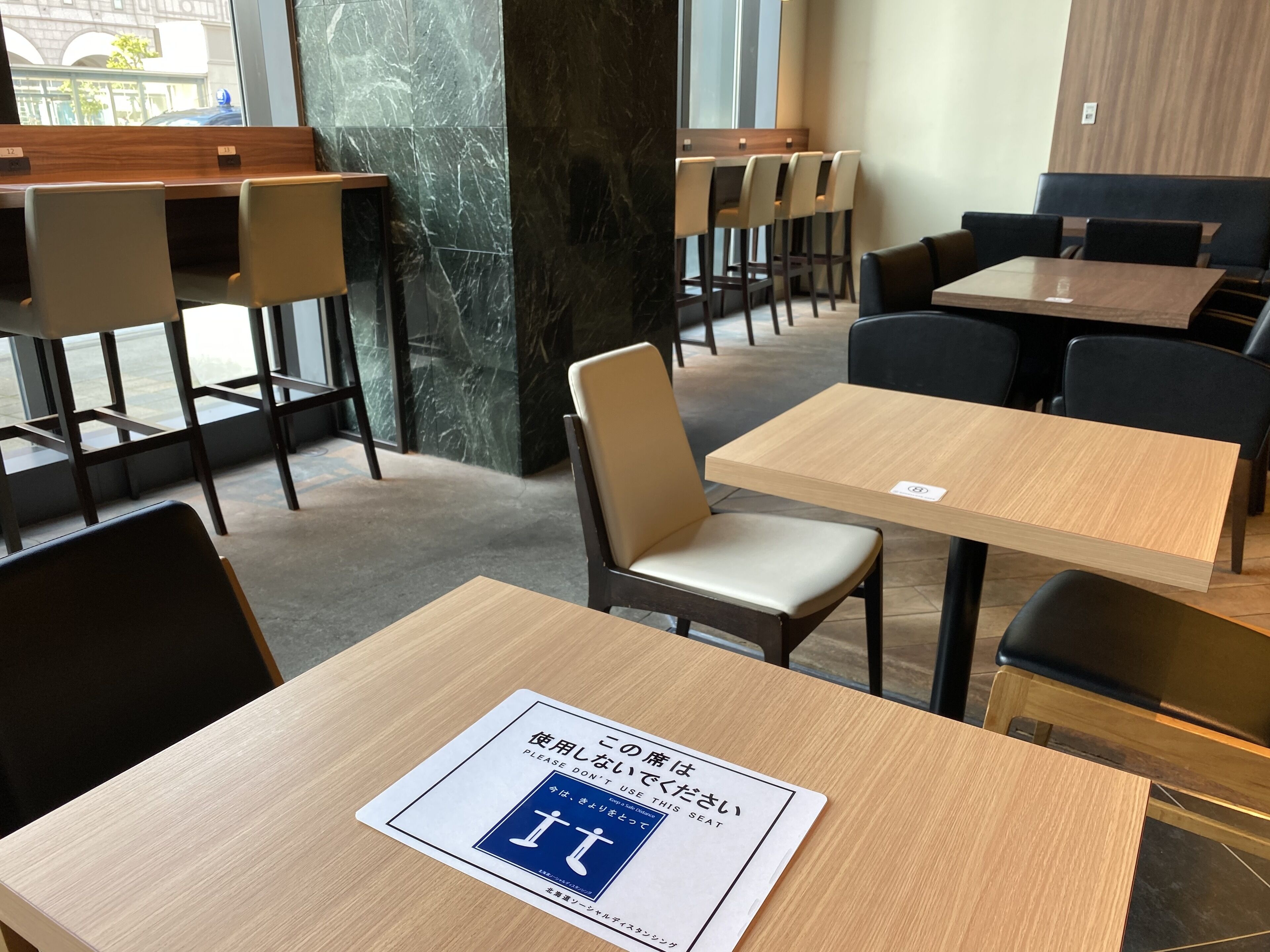 Interior moderno de restaurante com mesas e cadeiras de madeira, um pilar de mármore e um aviso indicando assento reservado.