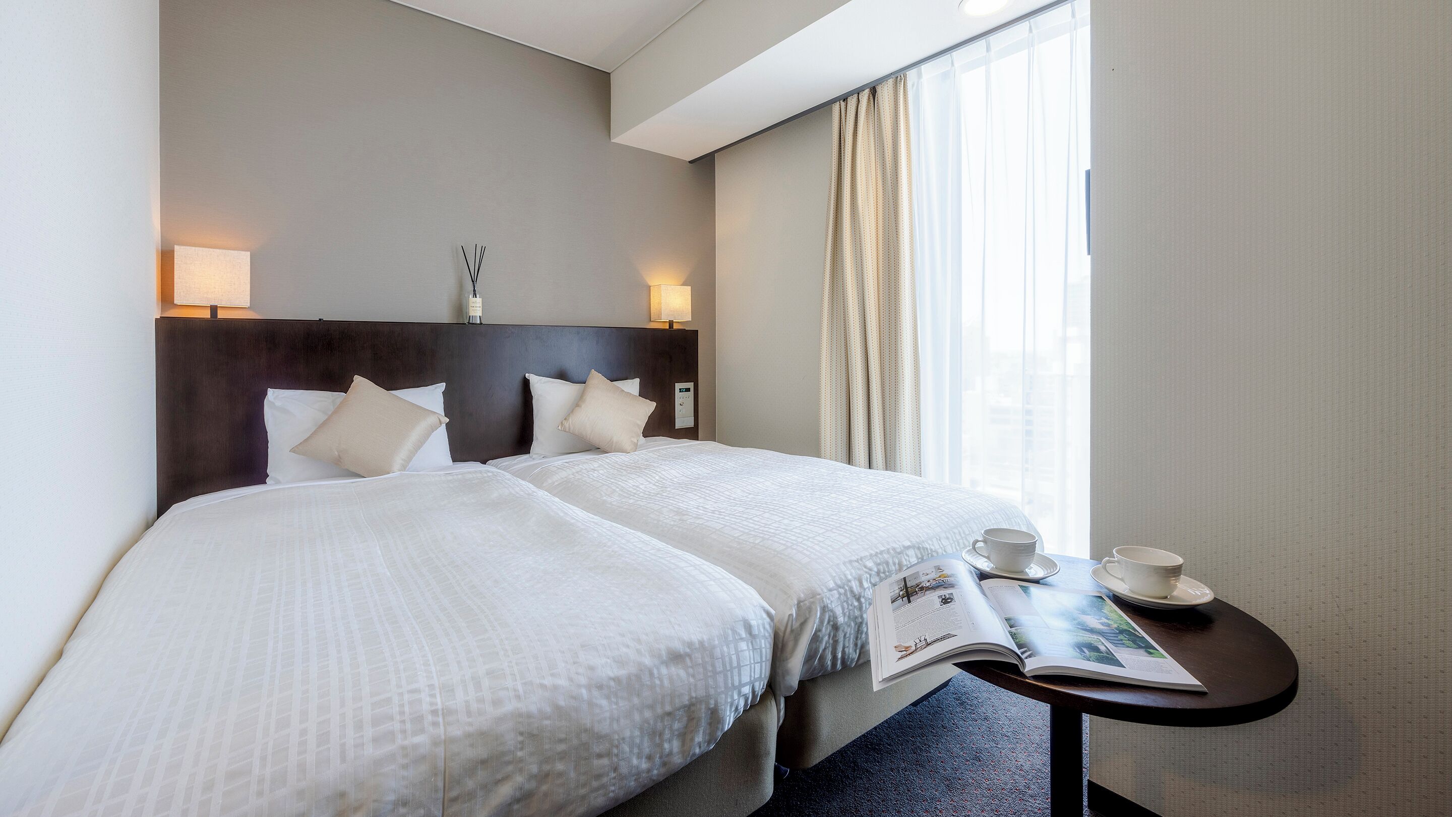 Une chambre d’hôtel avec deux lits, une table de chevet sur laquelle se trouvent un magazine, une tasse et un vase.