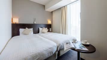 Une chambre d’hôtel avec deux lits, une table de chevet sur laquelle se trouvent un magazine, une tasse et un vase.